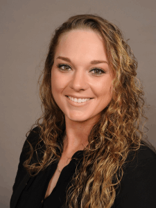 Professional photo of a female with blonde curly hair smiling and wearing a black collared shirt