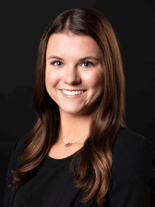 Professional photo of Brenna. She is a young woman with dark hair. She is dressed in business professional attire.