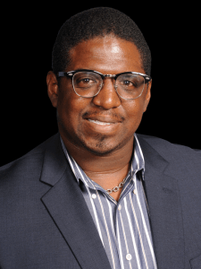 Professional photo of a male recruiter with short black hair wearing glasses, a striped shirt, and a black blazer