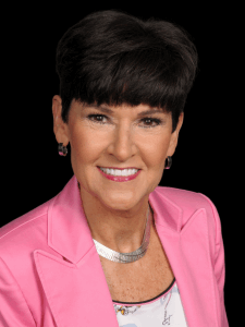 Professional photo of a female sales representative with short black hair wearing a white blouse, pink blazer, and silver necklace