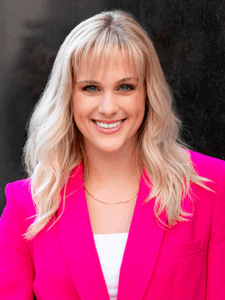 Professional photo of a young female marketing coordinator with mid-length blonde hair with bangs wearing a white top and bright pink blazer