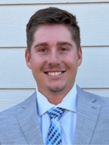 Professional photo of a young man in a grey blazer, white button-down, and blue patterned tie