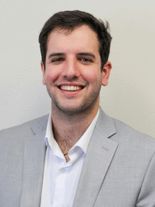 Professional photo of a young male skilled trade recruiter with short dark brown hair wearing a white button-down shirt and light grey blazer