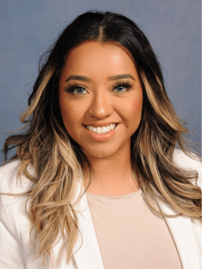 Professional photo of a young female senior on-site representative and light industrial recruiter with black and blonde hair wearing a tan top and white pink blazer