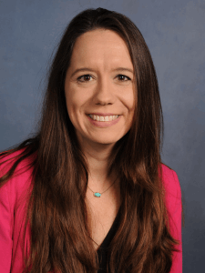 Professional photo of a female operations manager with long brown hair wearing a black top and bright pink cardigan