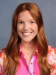 Professional photo of a young female office services and administrative recruiter with long red hair wearing a bright pink and orange floral button-down shirt