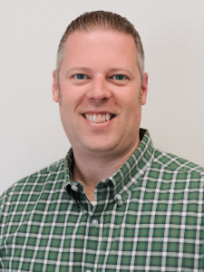 Professional photo of a male senior recruiter with grey hair wearing a green plaid button-down shirt