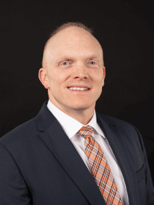 Professional photo of Adam dressed in business professional attire. Adam is a middle-aged man.