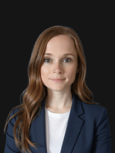 Professional photo of Tambi. Tambi is a young woman with reddish-brown hair. She is dressed in business professional attire.